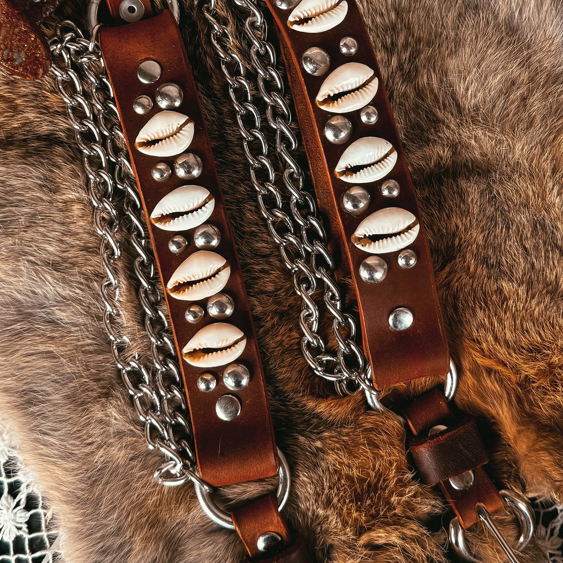 Brown leather straps with metal chain and shell-like embellishments on a fur surface.